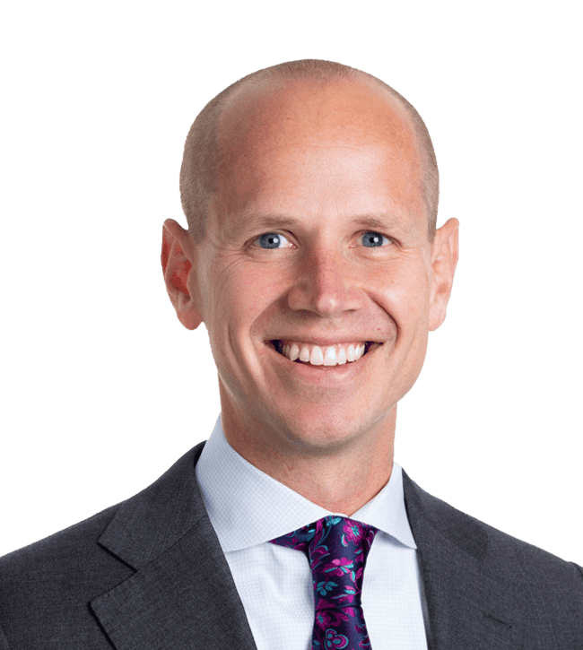 Head-and-shoulders portrait of a smiling bald man in a dark suit and purple patterned tie facing the camera.