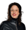 Laura-Fernandez Portrait of a smiling woman with shoulder-length dark hair, wearing a black leather jacket and red lipstick.